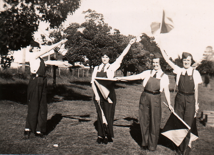Dressed in the practical green uniforms designed by McKenzie, Corps members spell out W E S C in flag semaphore