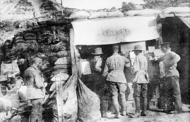 Four men queue to send or receive mail at the field post office at Anzac Cove, Gallipoli Peninsula. 1915.